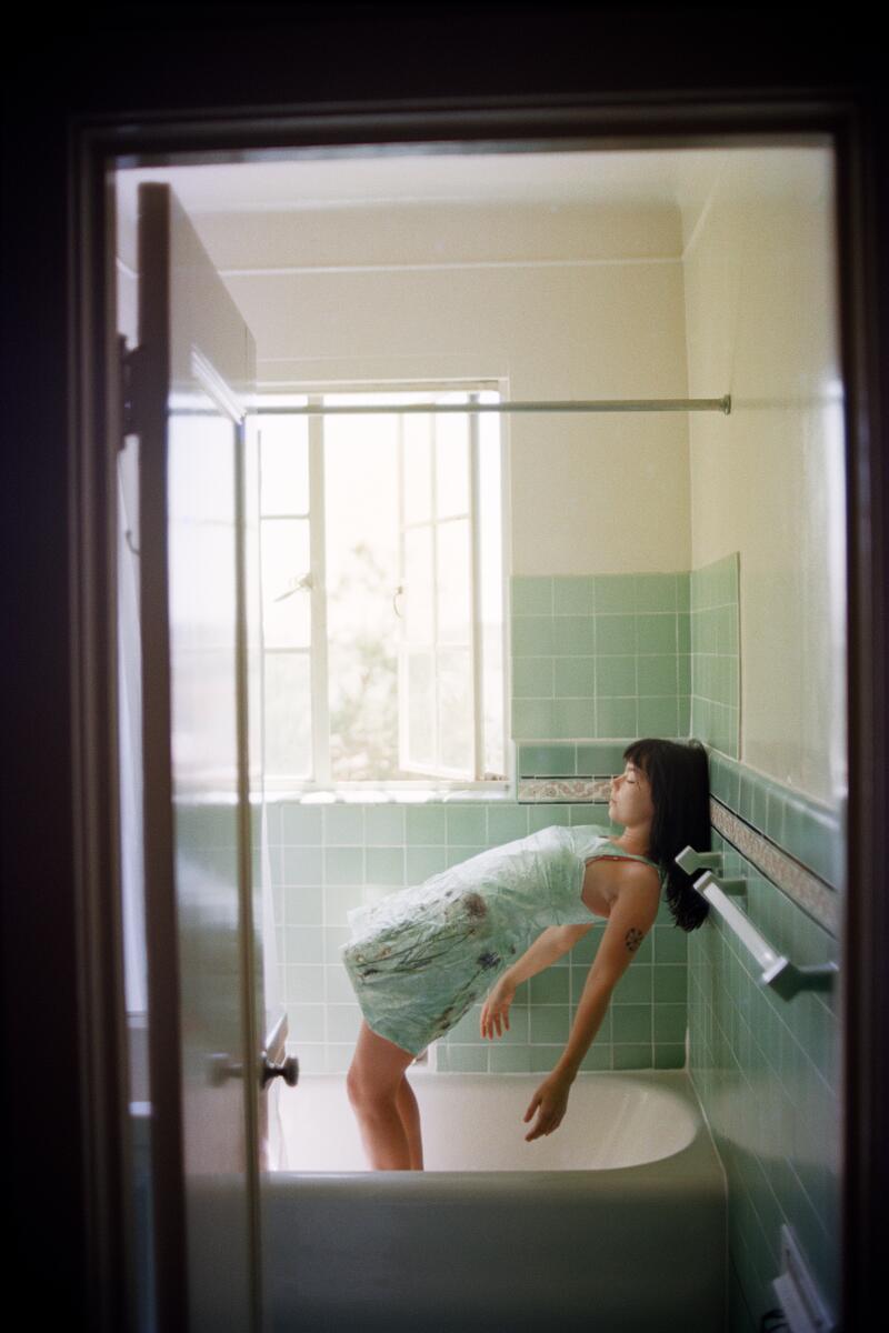 Seen through an open door, Bjork stands in a bathtub and leans back, her shoulders resting on a towel rack.