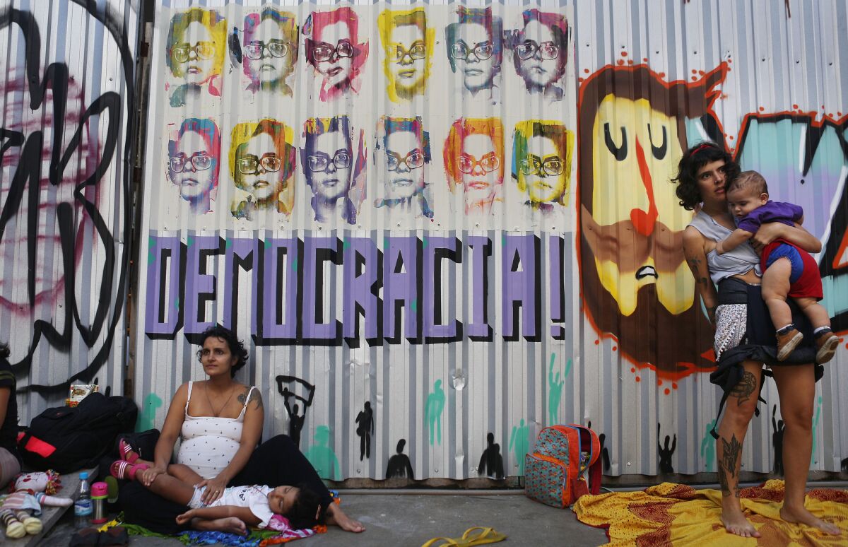 People gather at a protest against interim President Michel Temer in front of the currently shuttered Ministry of Culture, with grafetti depicting suspended President Rousseff and the word 'Democracy!', in Rio de Janeiro, Brazil. Artists have occupied the building, which was closed by interim President Temer, during a series of cuts to ministries by Temer after he assumed office.