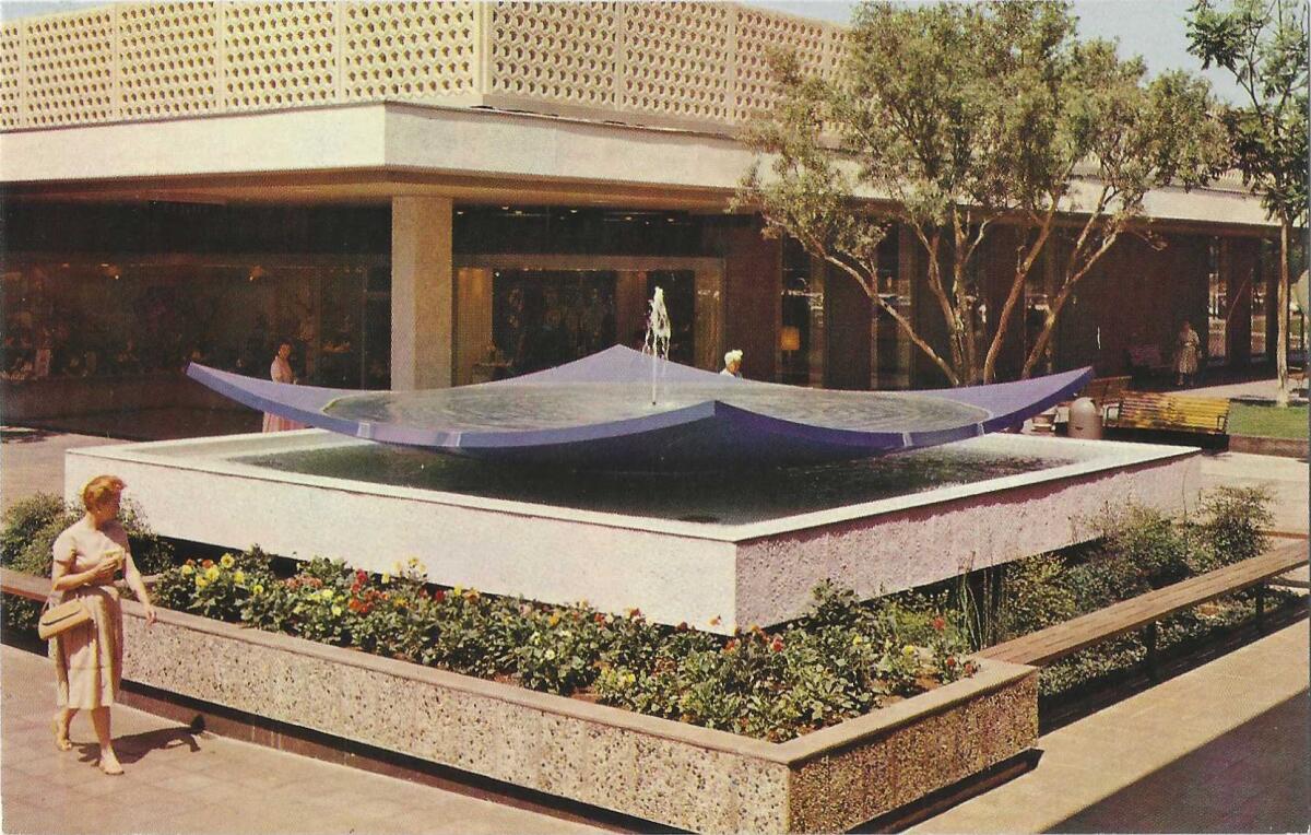 A woman walks past a geometric outdoor fountain at a mall on this vintage postcard scan.