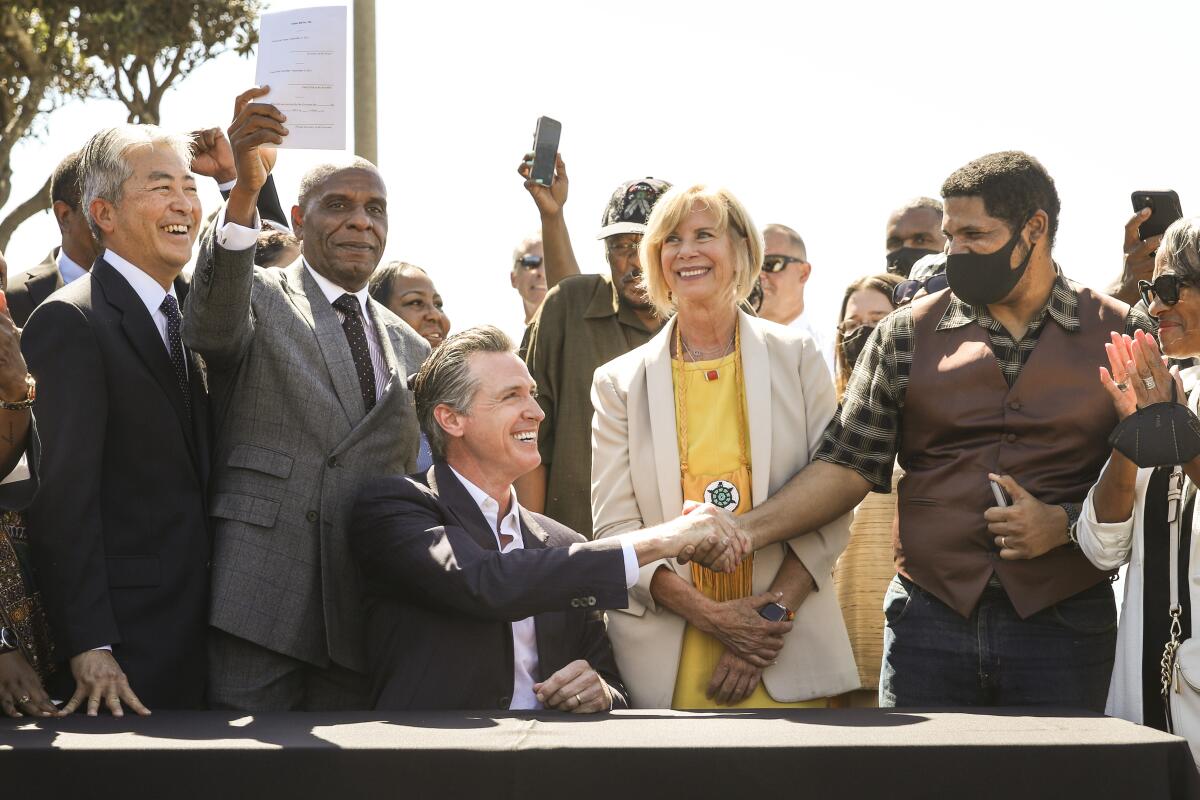 Gov. Gavin Newsom, seated with people behind him, shakes hands with a man.