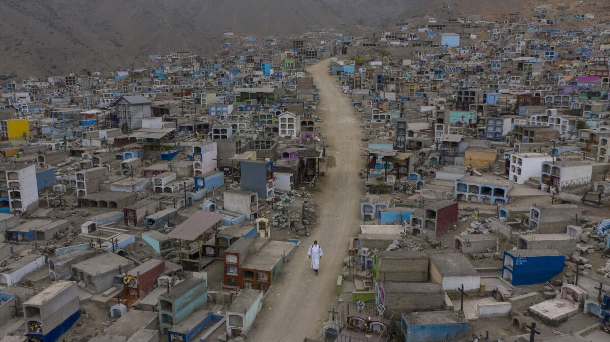 Brother Ronald Marin, a 30-year-old layworker from Venezuela, walks along a paved dirt road lined by graves, inside the "Martires 19 de Julio" cemetery in Comas, on the outskirts of Lima, Peru, Saturday, July 4, 2020. Wearing a white robe and shoes worn down by dust, Marin is one of the few who administers funerals in this cemetery far from the center of Peru's capital. (AP Photo/Rodrigo Abd)