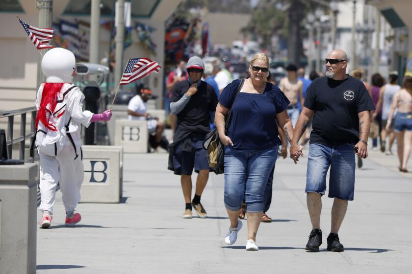 Angelina Franklin, 57 of El Monte, wears an astronaut costume as she waves American flags on the pier in Huntington Beach on Friday, June 26, 2020.