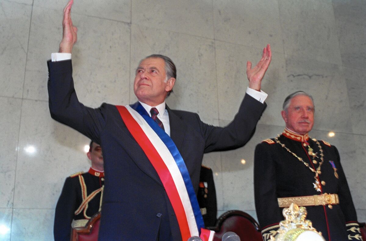 Patricio Aylwin, left, speaks after receiving the presidential sash at inaugural ceremonies in Santiago, Chile, in March of 1990 as outgoing President Augosto Pinochet looks on.