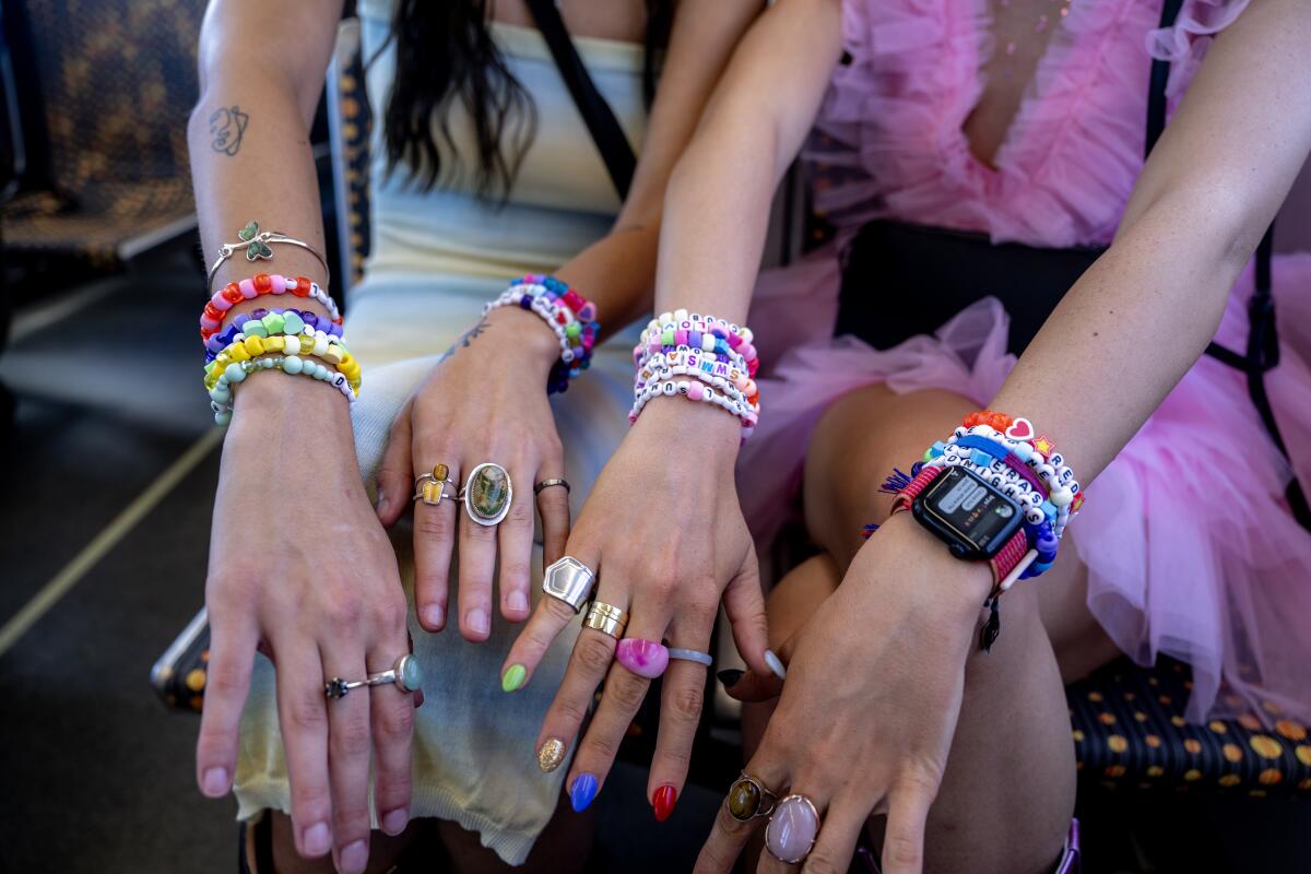 Two women show their bracelet jewelry while seated on a bus.