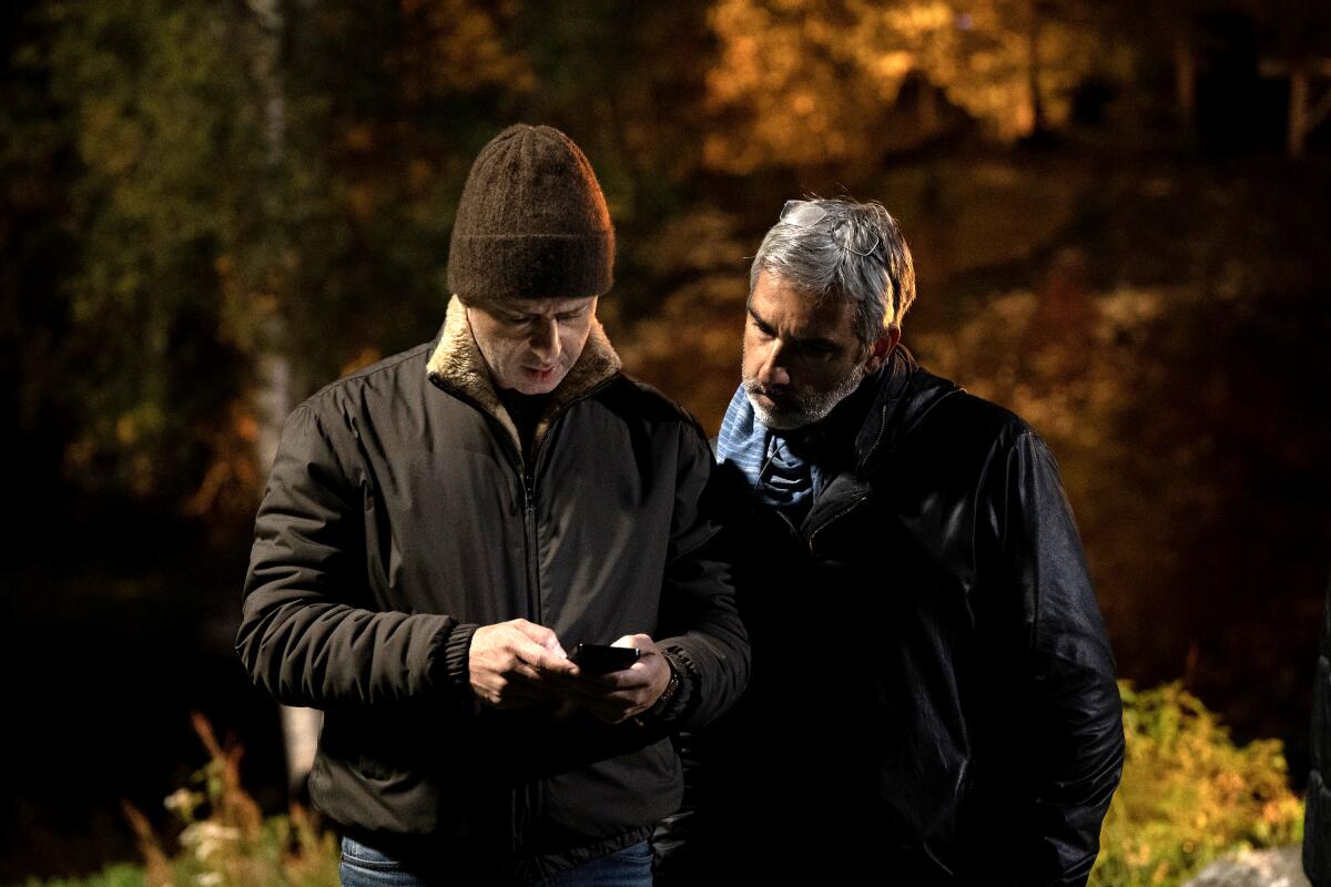 Two men in jackets stand outside looking at a cell phone.