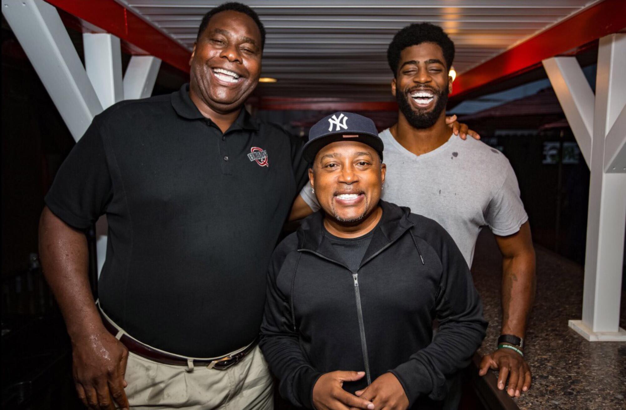 Al Baker, left, Daymond John and a third person smiling for a photo