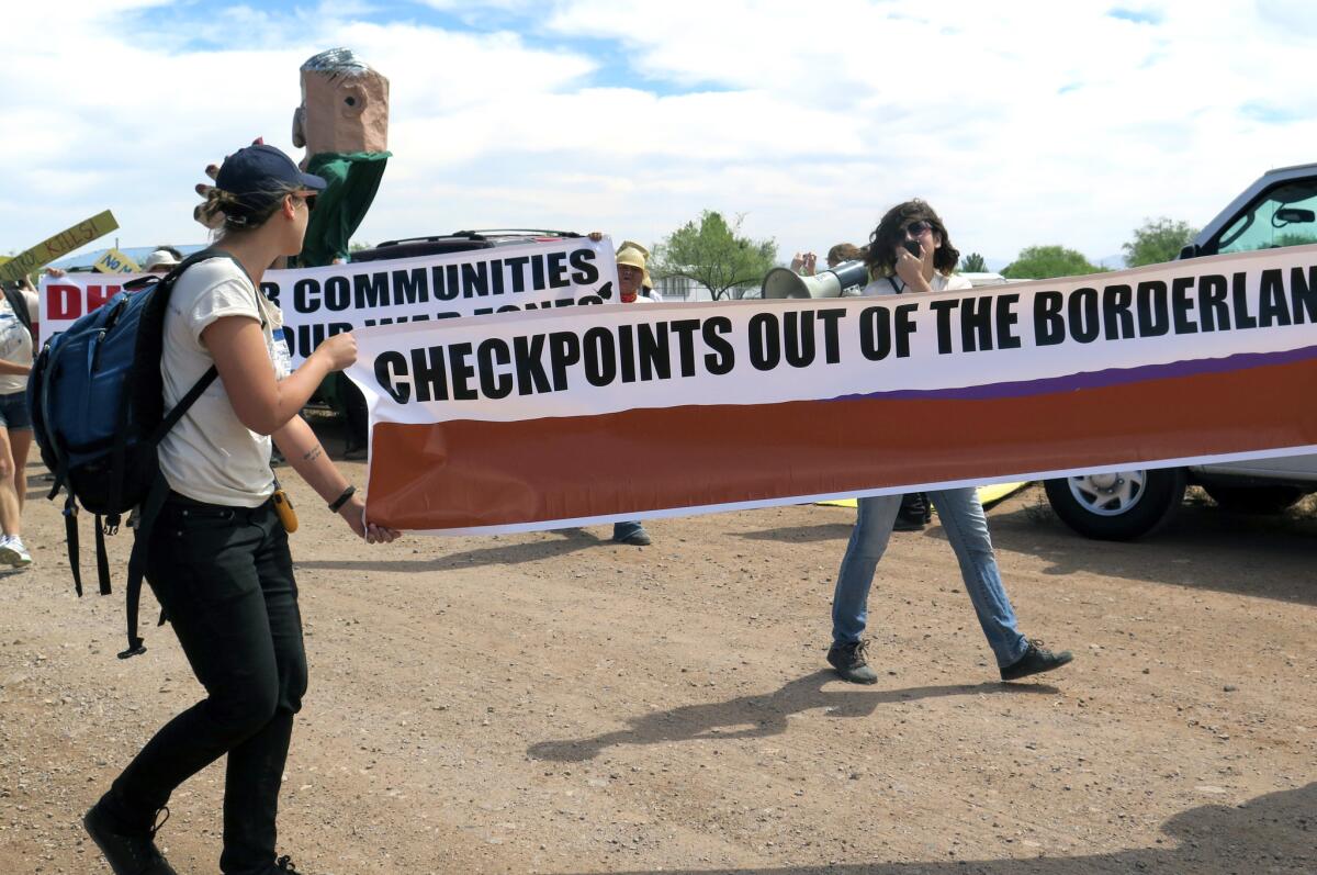 Dos manifestantes llevan una pancarta mientras caminan hacia un retén fronterizo en un camino en Amado, Arizona, el miércoles, 27 de mayo del 2015.