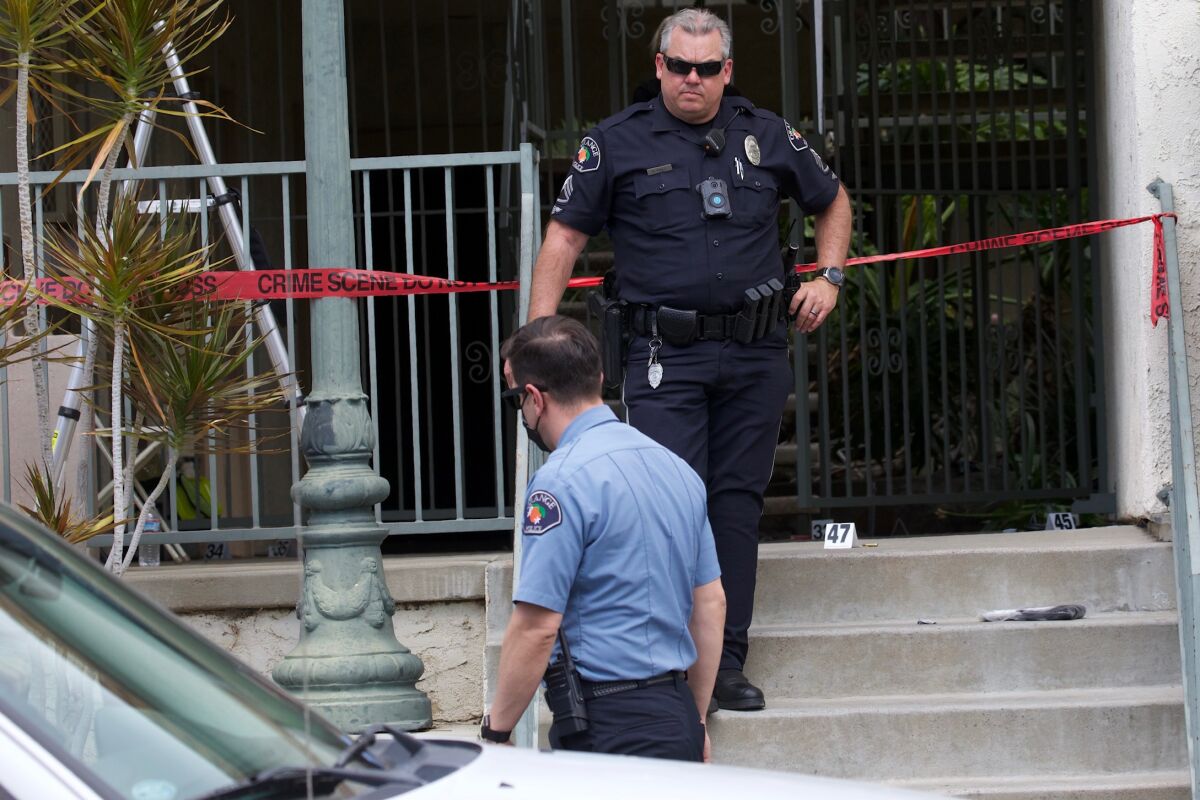 Two people in uniforms appear before a building entrance roped off with "crime scene" tape.