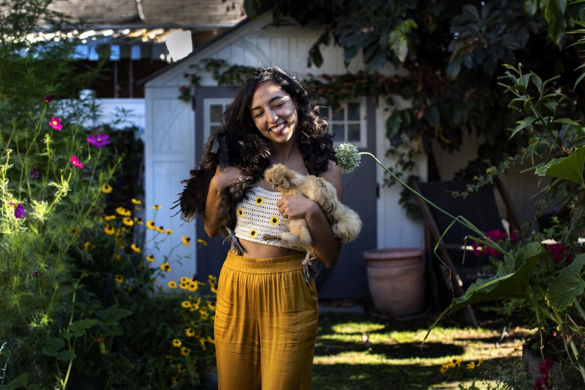 A woman holds a chicken in a garden. 