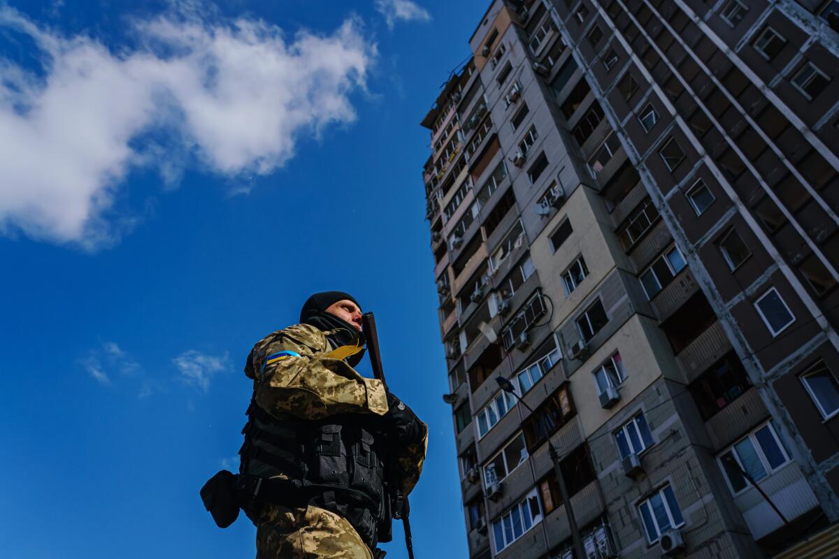A soldier stands guard outside a damaged apartment building 