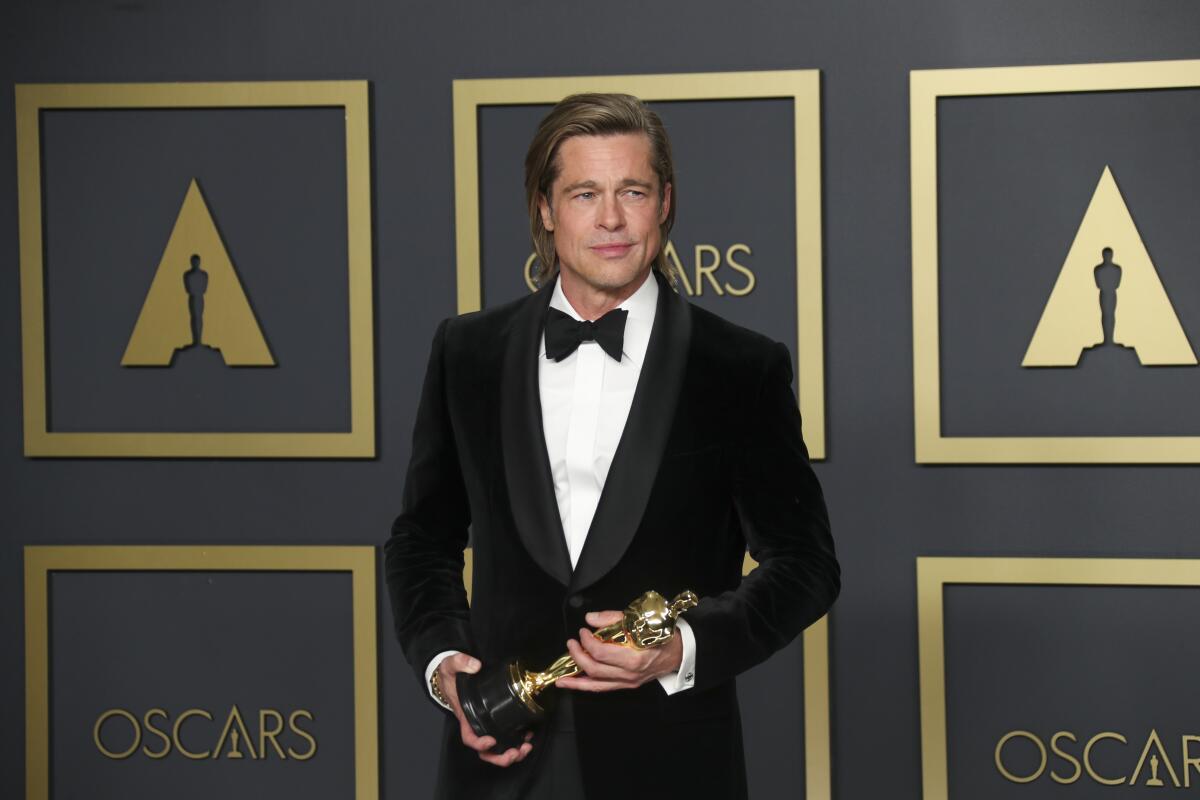 Brad Pitt, in a tux, poses for a photo holding an Oscar statuette.