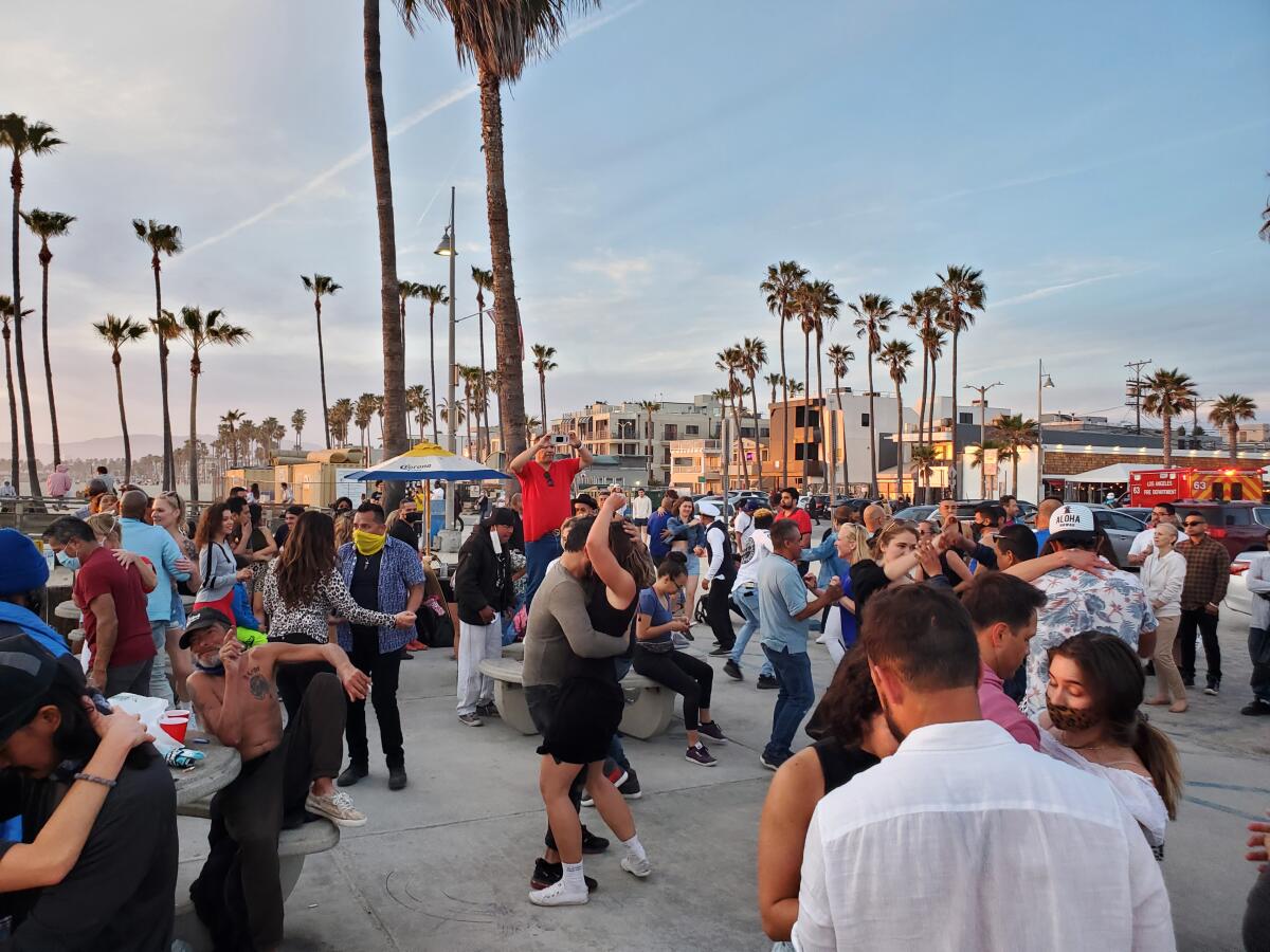 A crowd of people dance outdoors on a concrete patio amid palm trees.