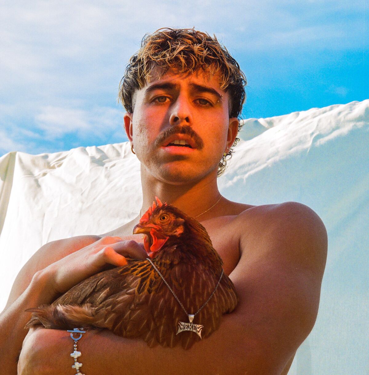 shirtless man holding a chicken with a necklace on