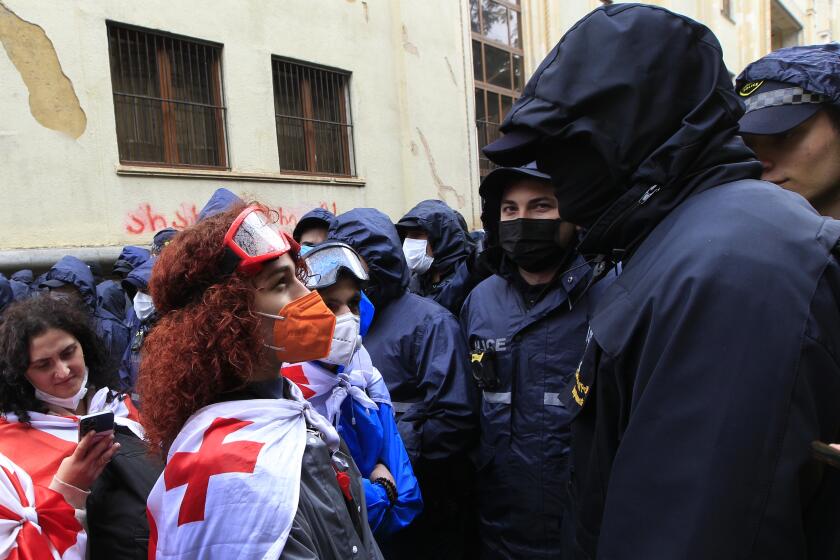 A demonstrator wears a national flag as she argues with the police that blocked the road towards the Parliament building during an opposition protest against "the Russian law" in the center of Tbilisi, Georgia, on Monday, May 13, 2024. Daily protests are continuing against a proposed bill that critics say would stifle media freedom and obstruct the country's bid to join the European Union. (AP Photo/Shakh Aivazov)