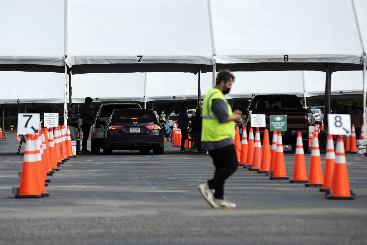 A man in a yellow reflective vest walks by orange cones in a nearly empty parking lot.
