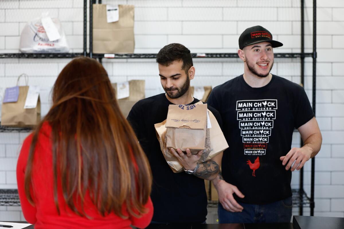 Colony manager Sean Aslany, center, hands a pickup order from Trejo's Tacos to a customer as Calvin Skarlat of Main Chick Hot Chicken talks to a customer at Colony.