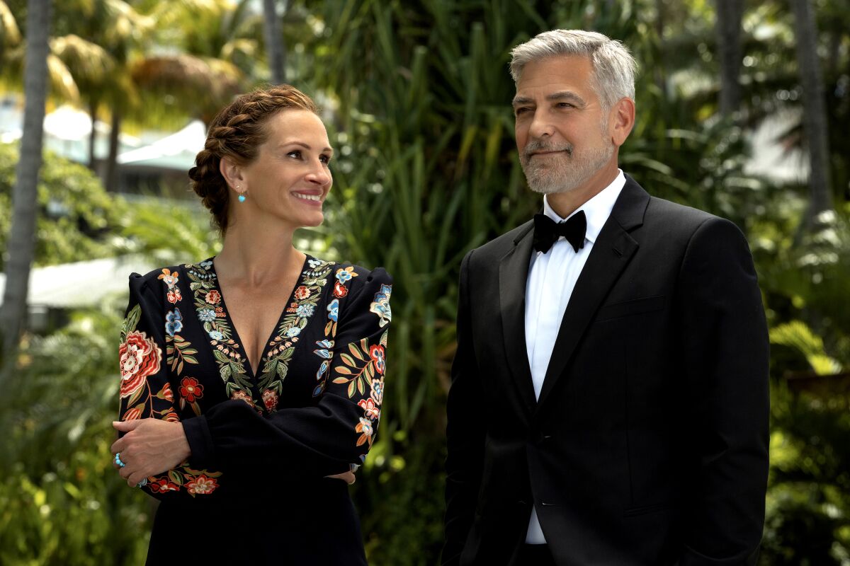 A woman in an embroidered dress smiles at a man in a tuxedo.