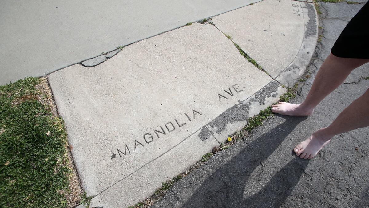 Mike Elliott stands at Ninth Street and Pecan Avenue in Huntington Beach, where the curb is embossed with "Magnolia Avenue," Pecan's former name. Elliott has asked the city to preserve its few remaining similar pieces of history.