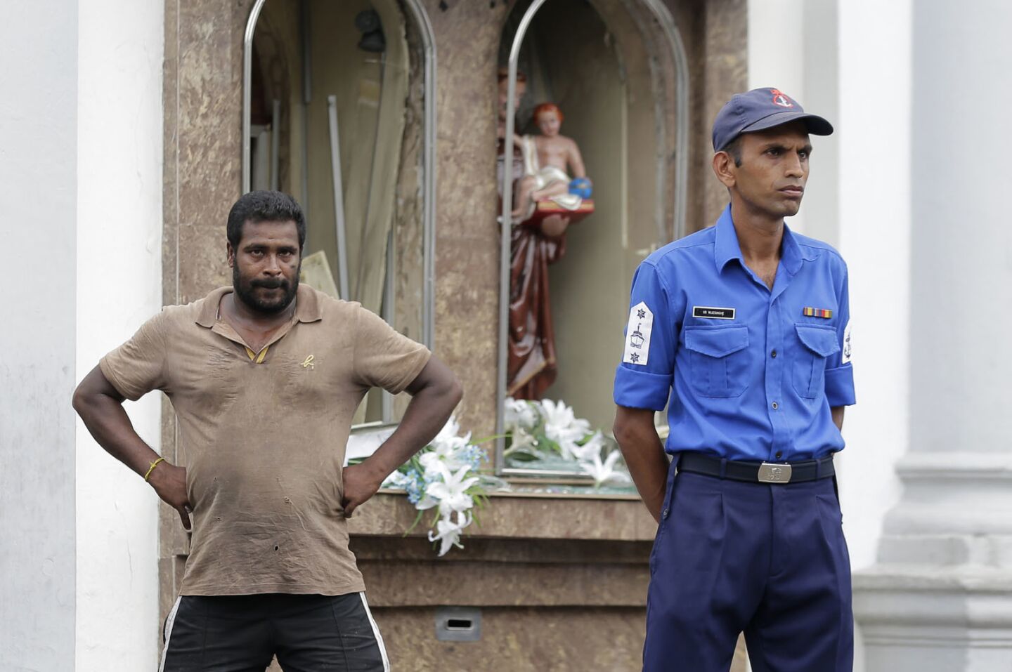 A Sri Lankan police officer and a local stand outside St. Anthony’s Shrine after an explosion April 21.