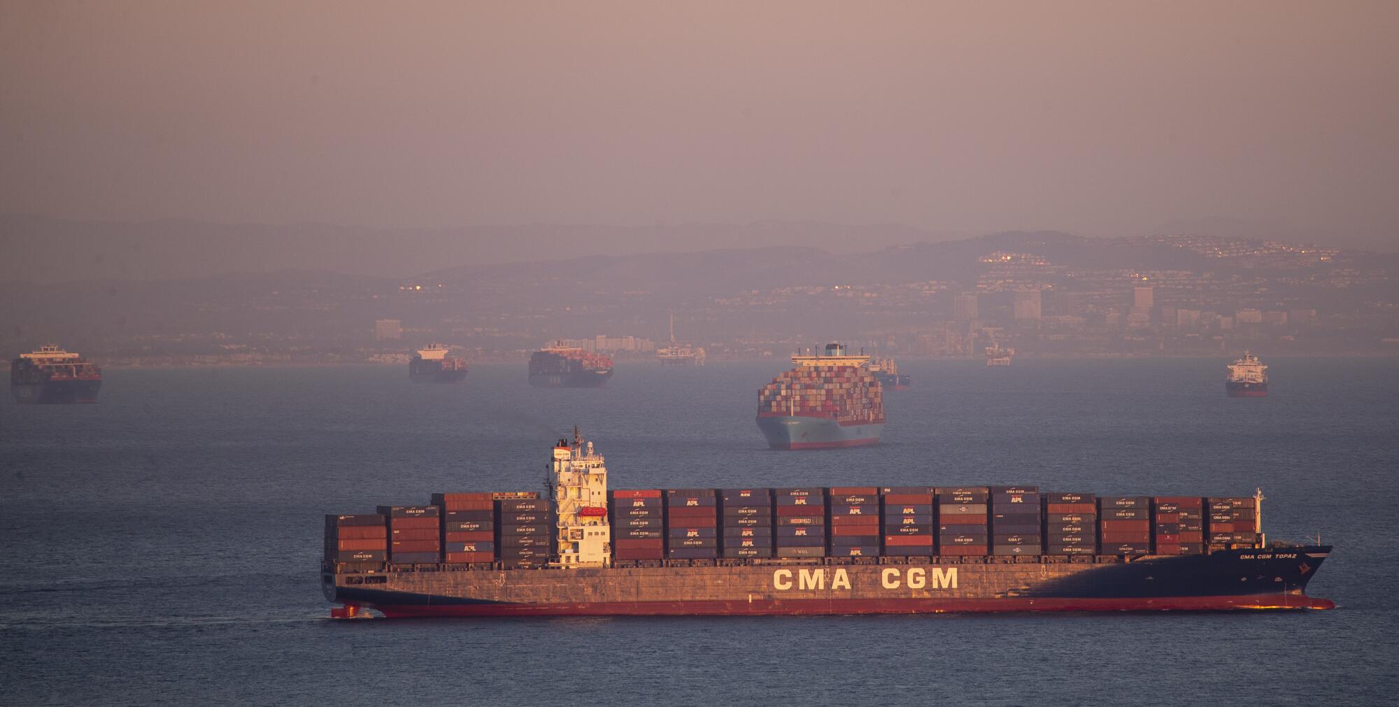 A container ship is seen in the foreground on the water with others in the distance