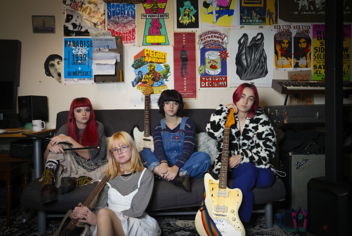 A teen rock band sitting on a couch holding guitars and instruments