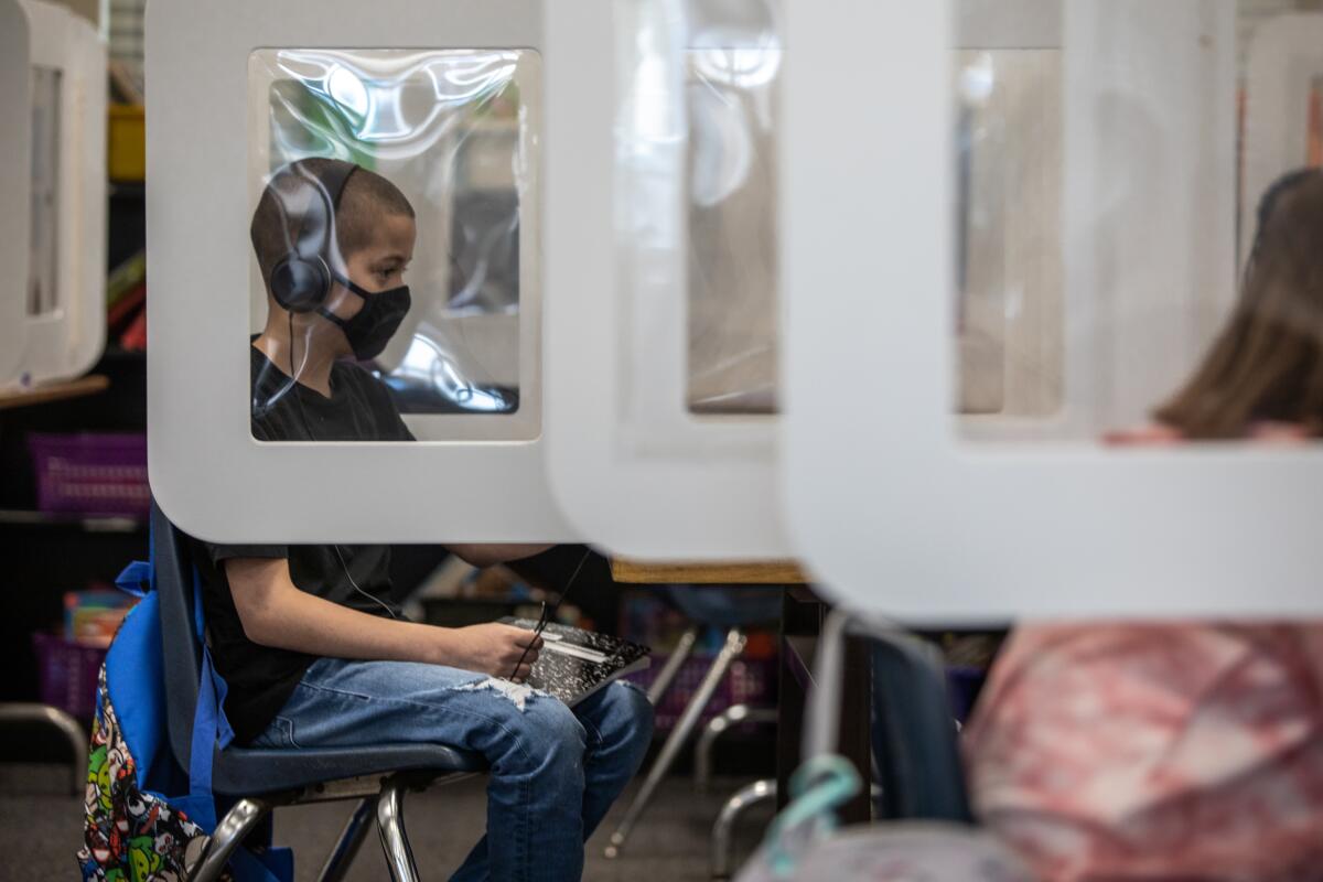 A boy sits behind a desk partition and wears headphones to listen to a teacher's lesson at Perkins K-8 school.