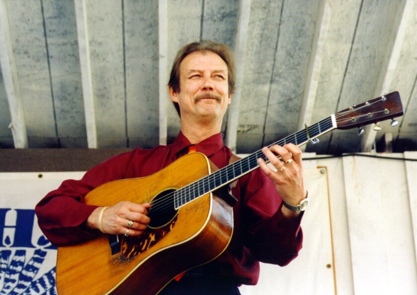 Tony Rice is shown around 2000 smiling and strumming on a guitar.