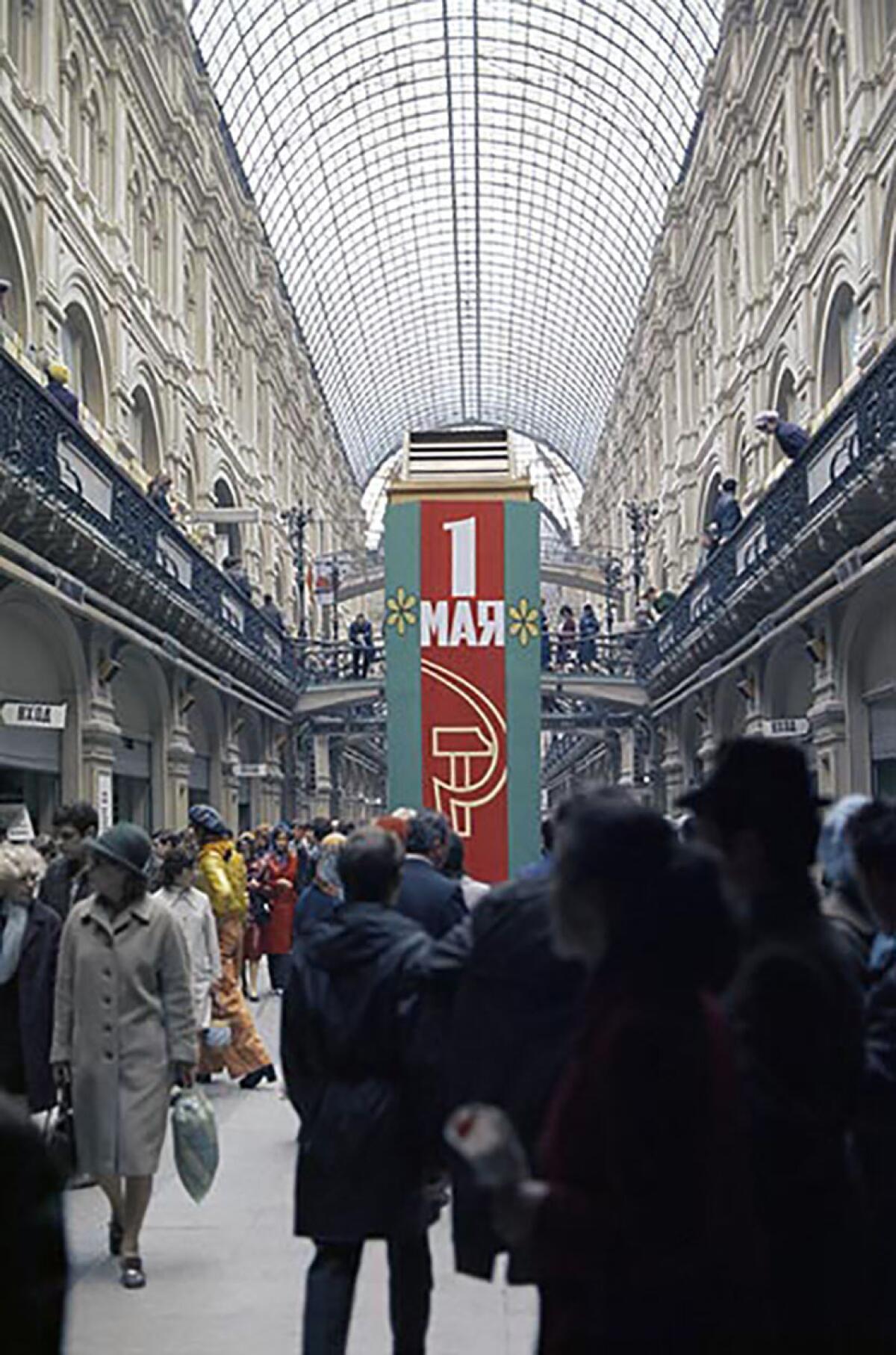 People in a store. In the background is a large red banner with a hammer and sickle and May 1 in Russian letters.  