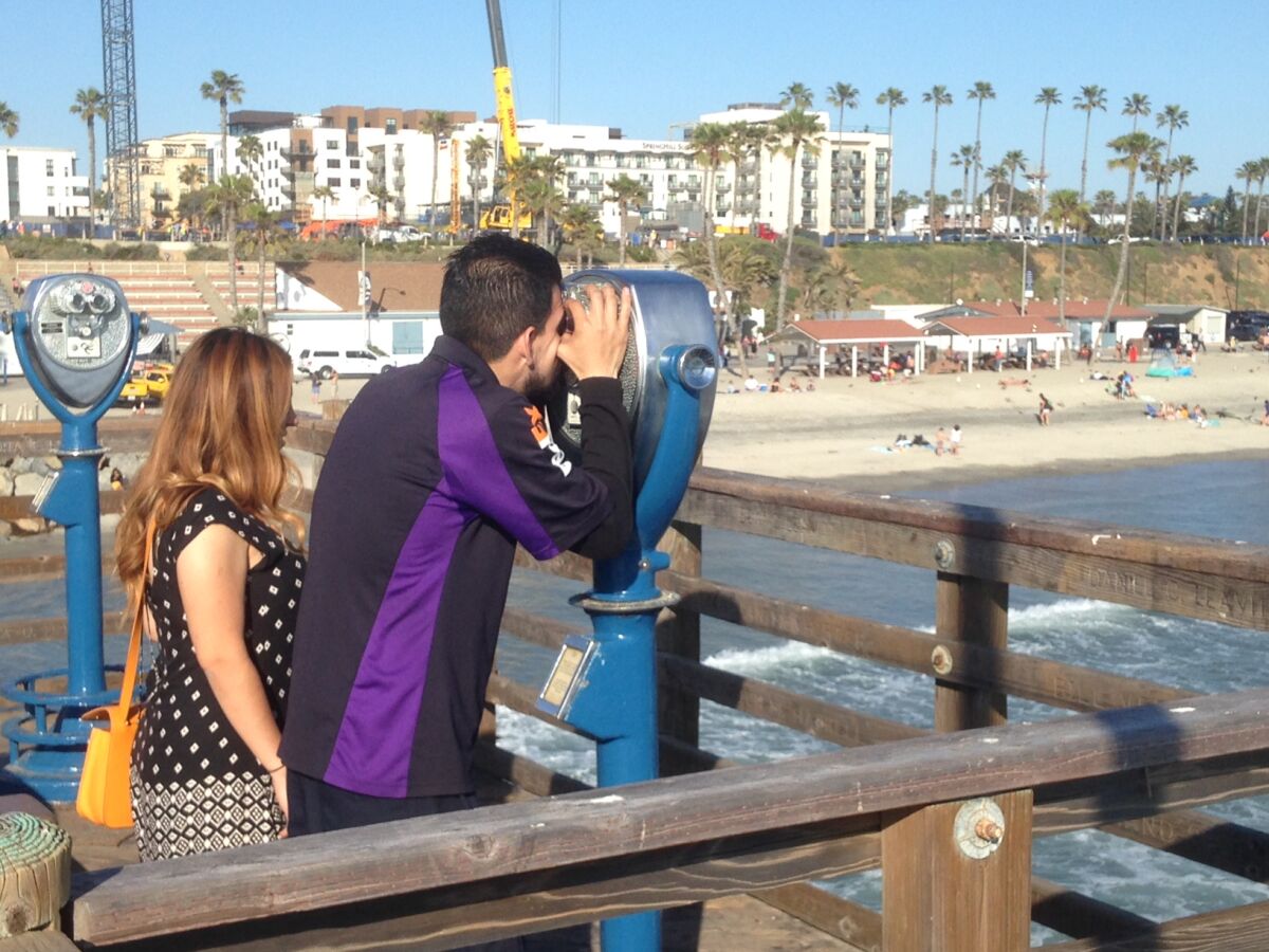 Wesley Riano and Paola Lastiri take turns looking through binoculars on the Oceanside pier.