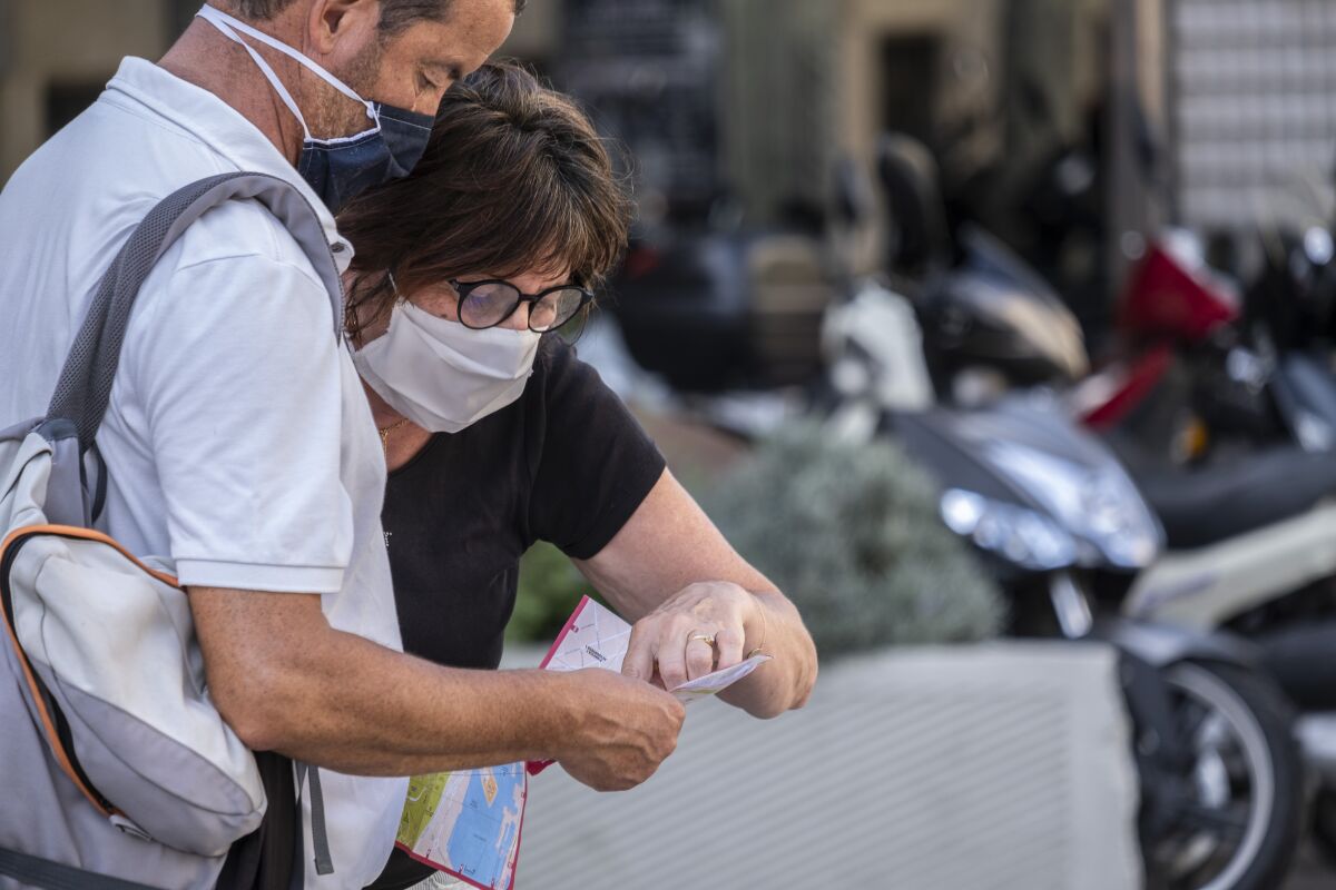 A tourist couple wearing facemasks consult a map of the city of Barcelona 