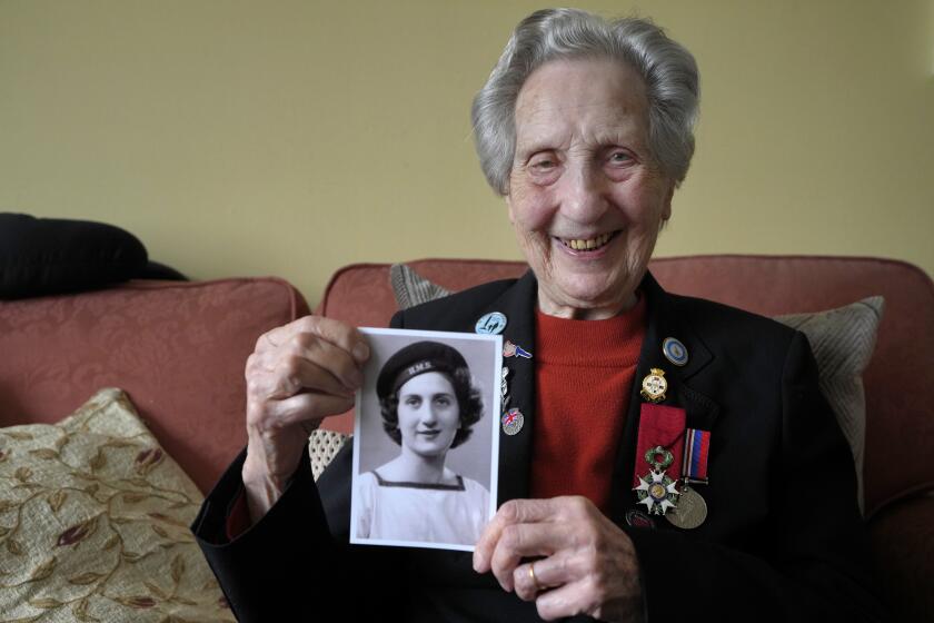 Marie Scott who was a serving Wren and switchboard operator at the time of D-Day, holds up a photograph of herself in 1944, at her home in London, Thursday, April 25, 2024. D-Day, took place on June 6, 1944, the invasion of the beaches at Normandy in France by Alied forces during World War II. (AP Photo/Kirsty Wigglesworth)