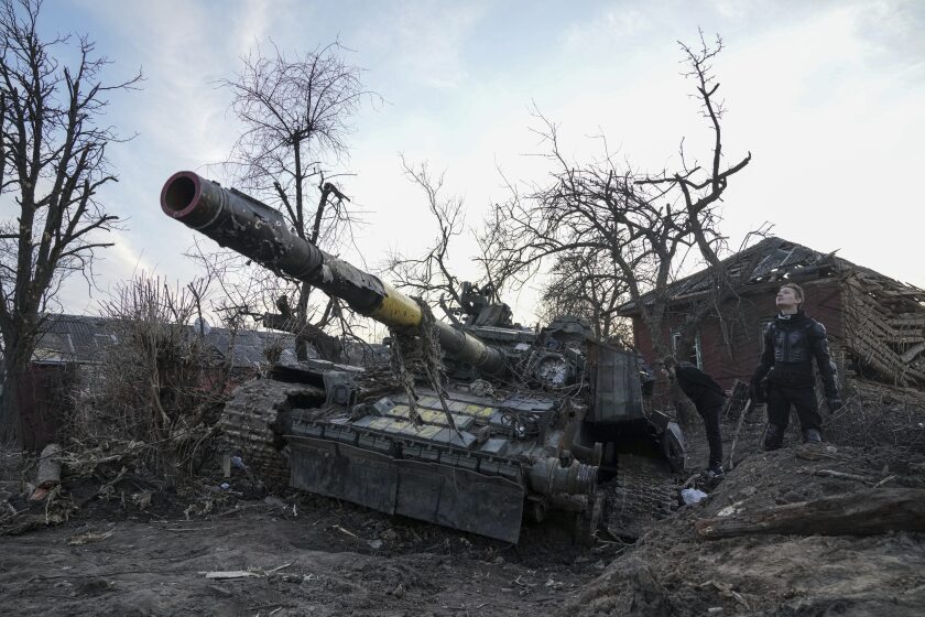 مردان در کنار تانک ویران شده در چرنیهیو اوکراین ایستاده اند.