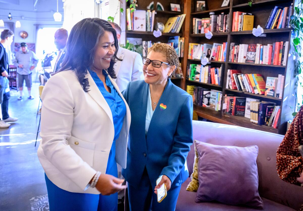 Mayor London Breed and Mayor Karen Bass stand together with bookshelves in the background