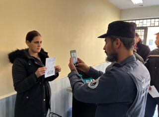A man uses a cellphone to photograph a woman in dark clothes holding a white paper