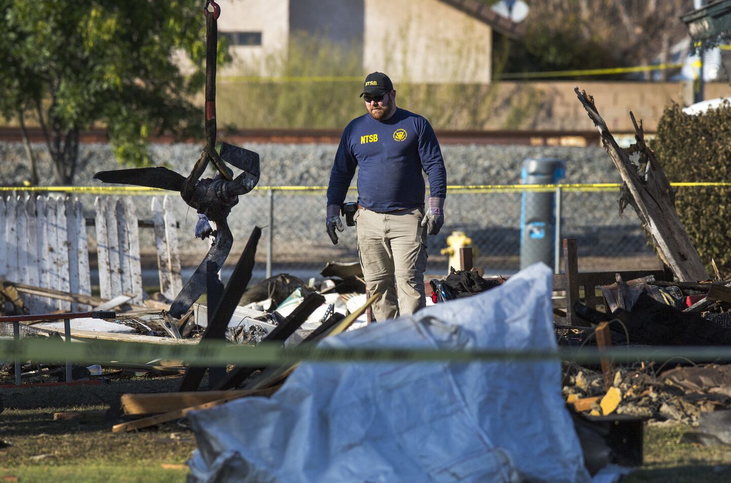 An NTSB agent watches as a small hoist lifts a propeller out of the front-yard wreckage the day after a small plane crashed into a Riverside home, killing three people.