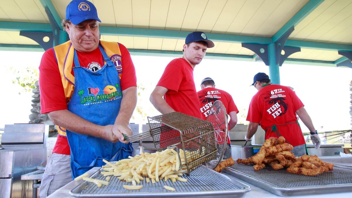 Rick Blake, left, unloads a fresh batch of french fries as fellow cook Vincent Williams, center, lays out a batch of fresh Alaskan cod during a past Costa Mesa-Newport Harbor Lions Club Fish Fry. This year is the Fish Fry's last at Fairview Park. It will move back to Lions Park in 2020.