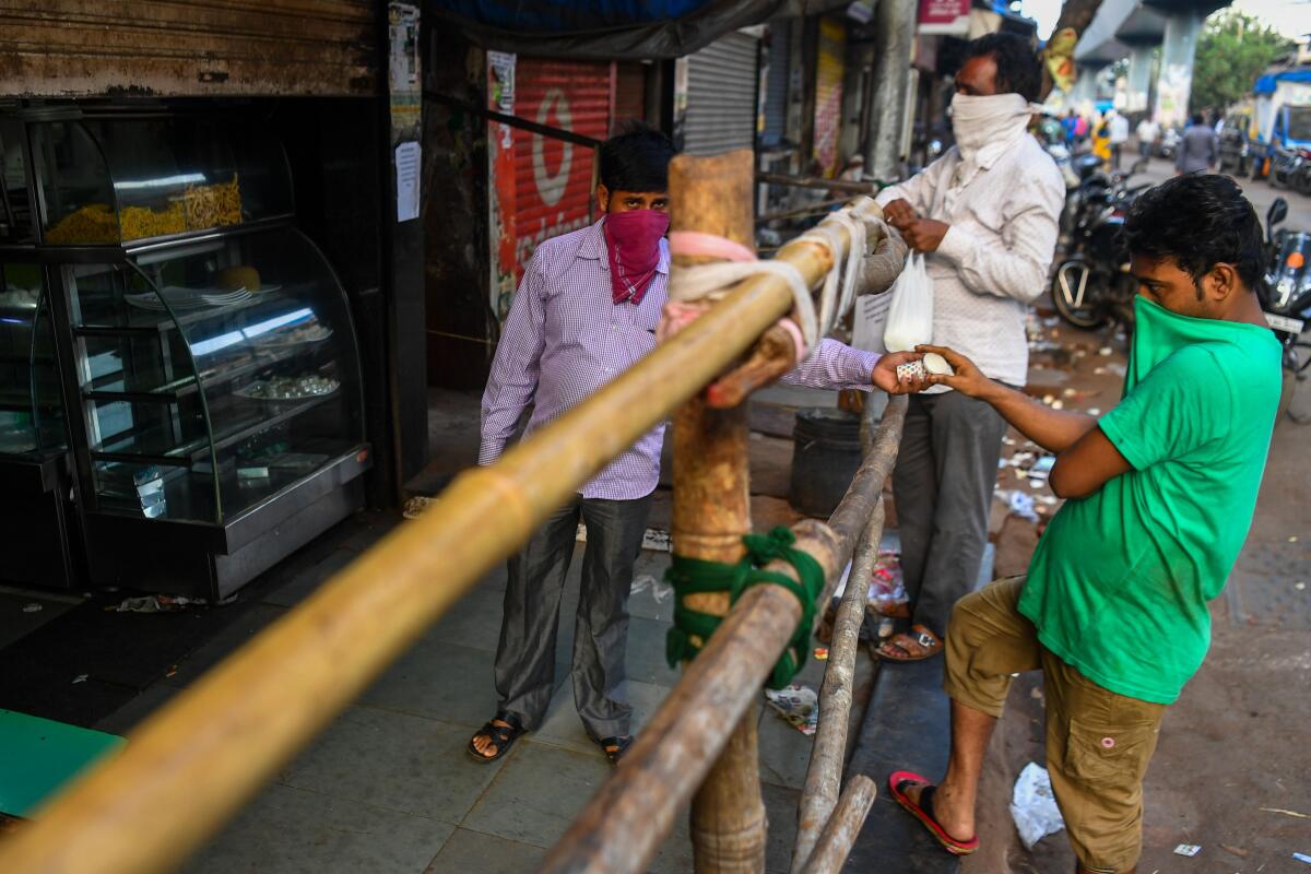 A tea seller hands cups to a customer from behind a barricade to preserve social distancing inside the Dharavi slum of Mumbai, India.