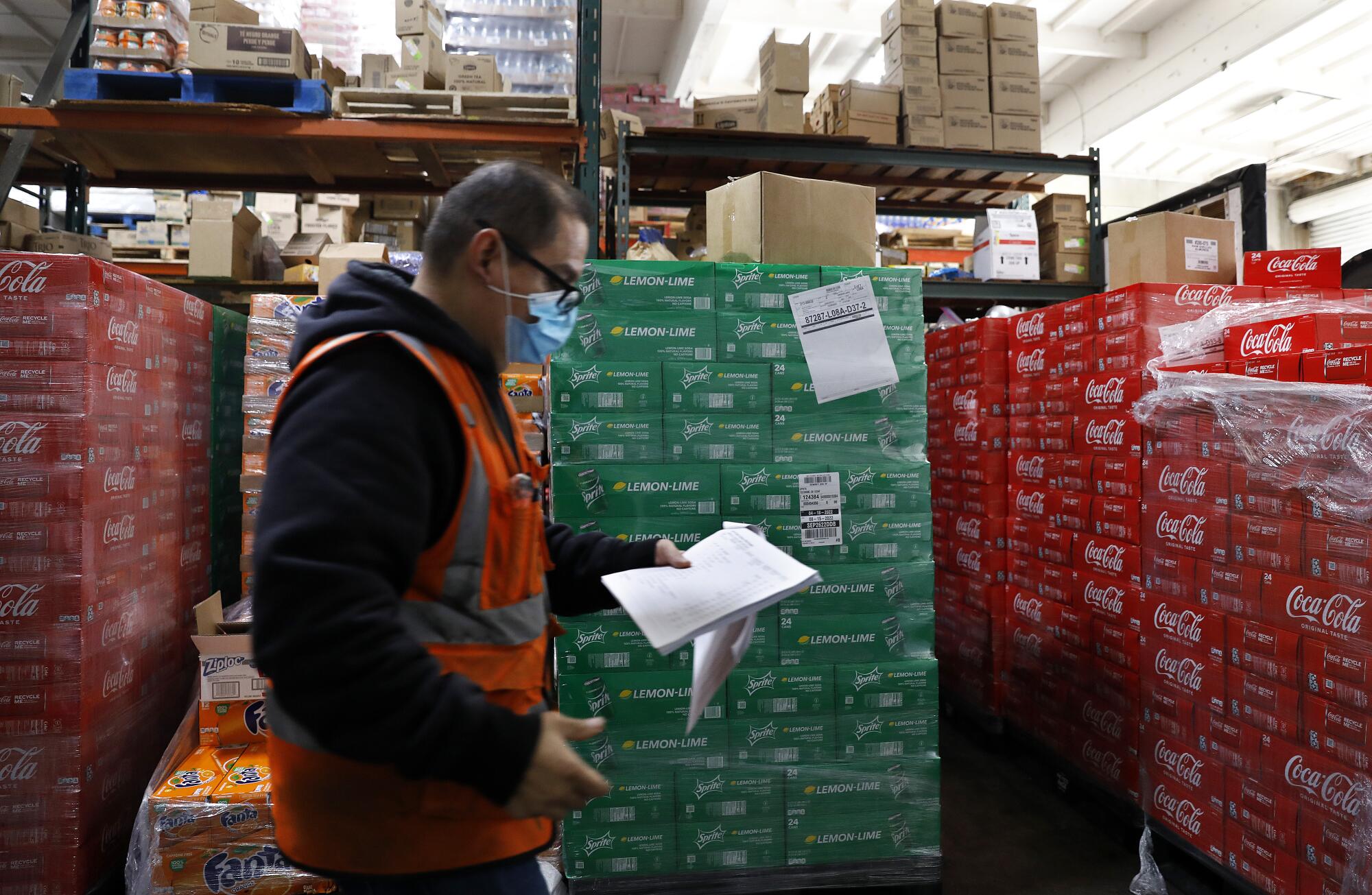 A man checks a list next to pallets of sodas.