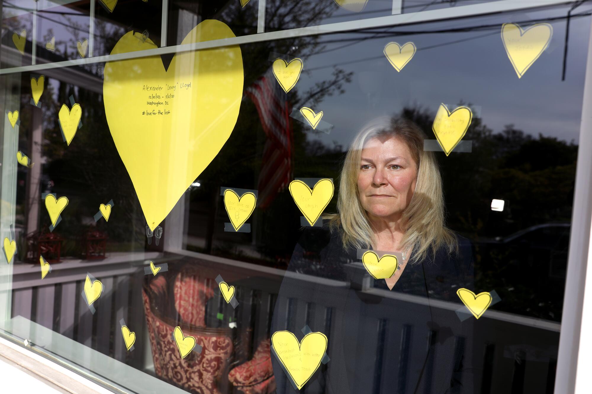 A woman stands behind a window with several yellow paper hearts taped to it