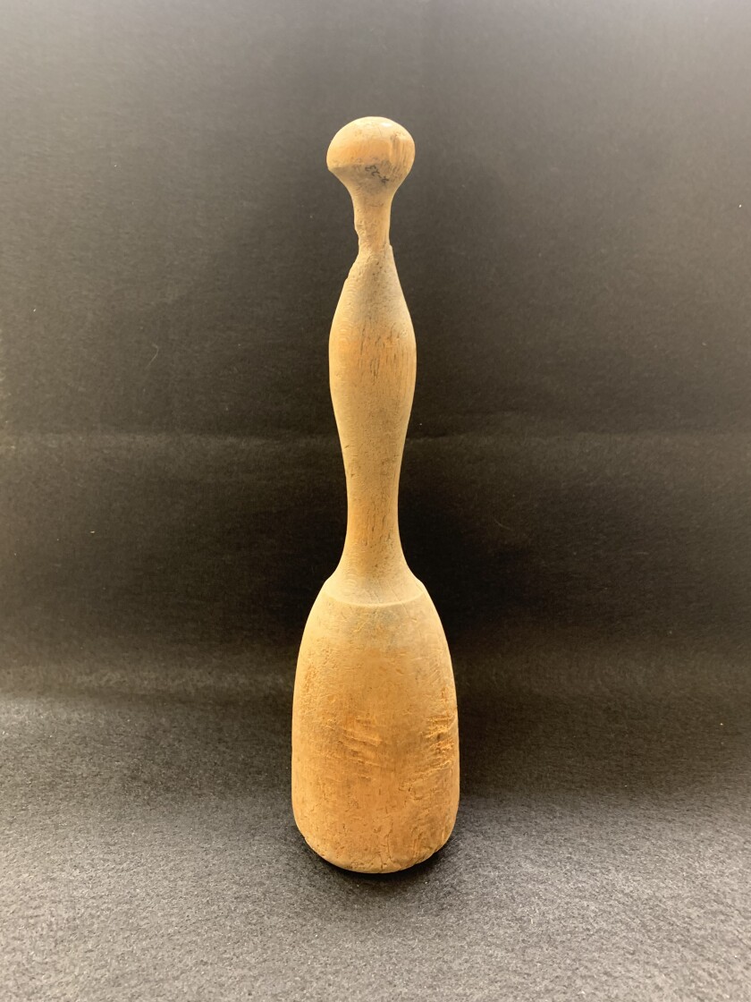 A wooden potato masher is shown standing vertically against a charcoal-colored background.