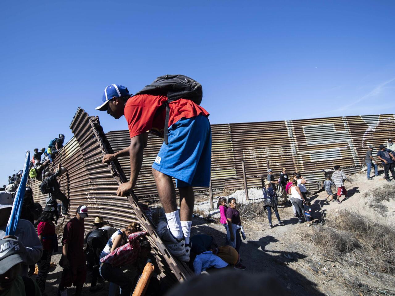 A group of Central American migrants -- mostly Hondurans -- climb a metal barrier on the U.S.-Mexico border in Tijuana.