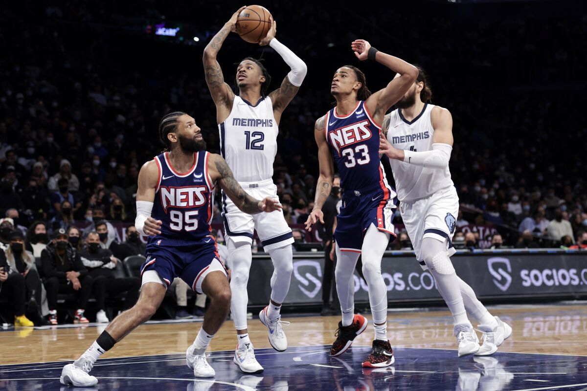 Memphis Grizzlies guard Ja Morant (12) drives to the basket between Brooklyn Nets forward Nic Claxton (33) and guard DeAndre' Bembry (95) during the first half of an NBA basketball game Monday, Jan. 3, 2022, in New York. (AP Photo/Adam Hunger)