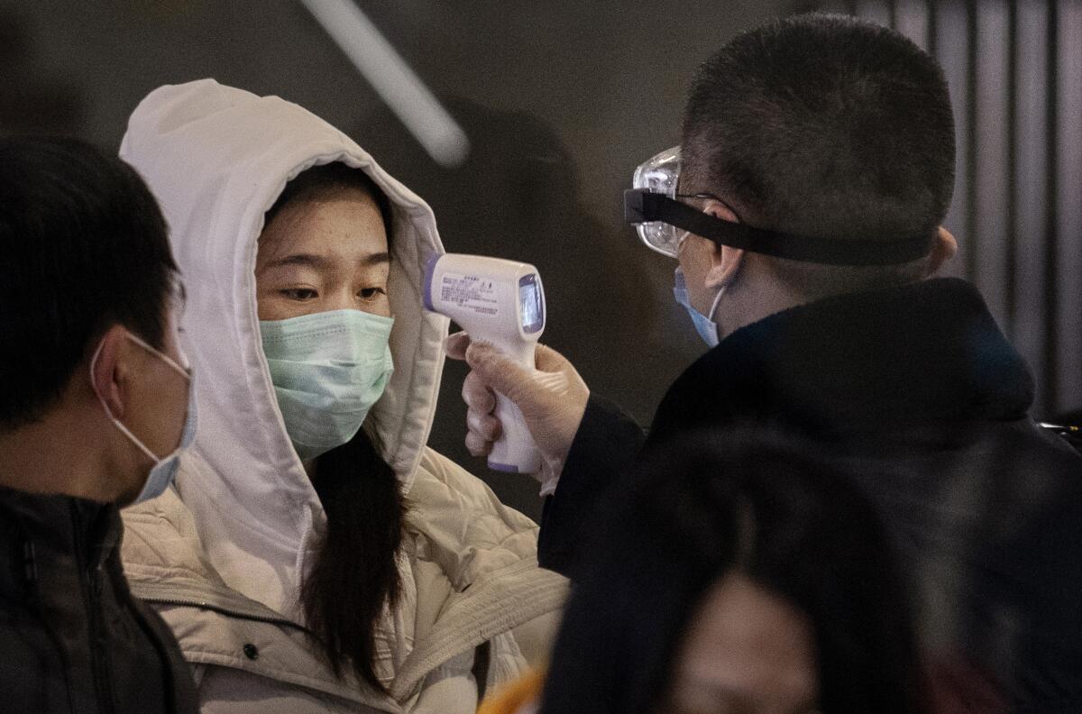 A woman who just arrived on the last bullet train from Wuhan to Beijing is checked for a fever by a health worker at the railway station.