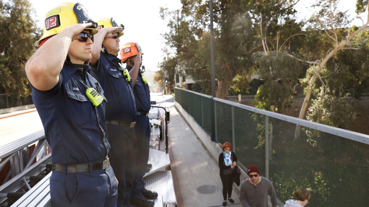 Burbank firefighters including Rich Dunn, left, salute from an overpass in Burbank as a procession for Cal Fire Engineer Cory Iverson, 32, passes through in route to San Diego.