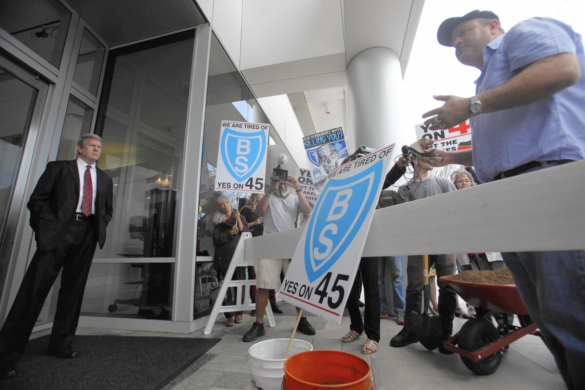 Jamie Court, right, Proposition 45’s author and president of Consumer Watch, appeals to security guards to deliver buckets filled with steer manure to health insurer Blue Shield's offices in El Segundo.