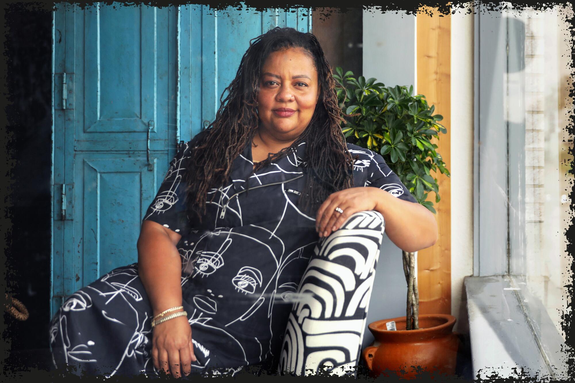 woman in a black patterned dress sits in black and white patterned chair
