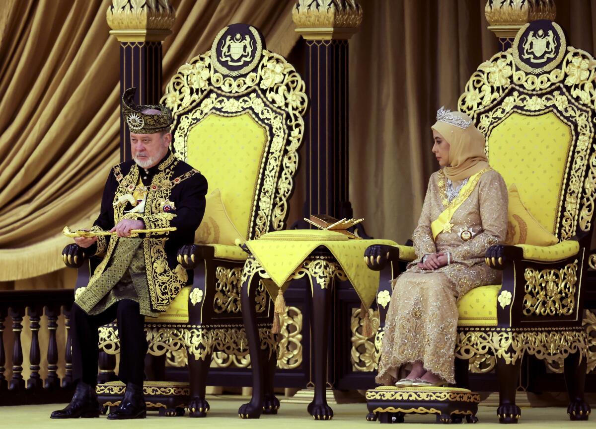 A man and woman in ornate clothing sit on thrones.