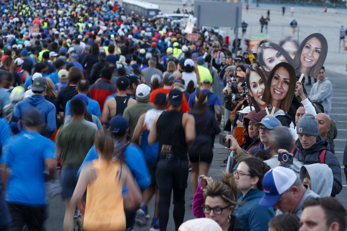 A spectator holds cardboard cutouts of a woman's face as L.A. Marathon runners pass.