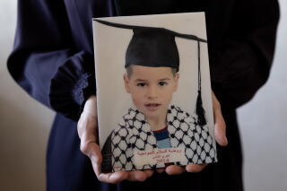 A pair of hands holding a photo of a child with a graduation cap and a kaffiyeh scarf