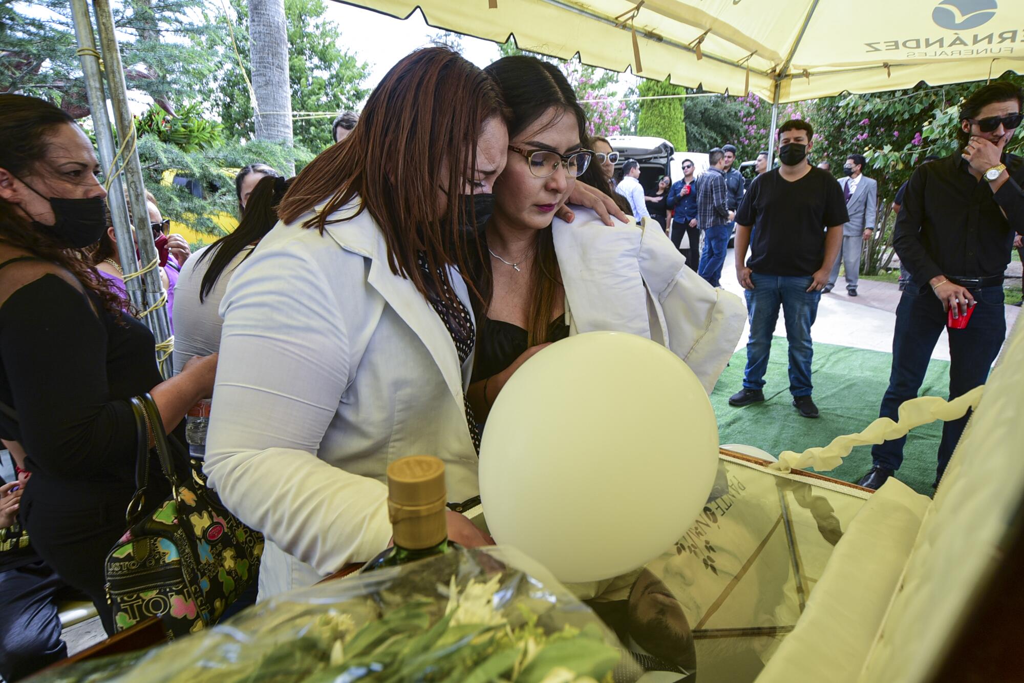 Two women embrace as they stand over a casket
